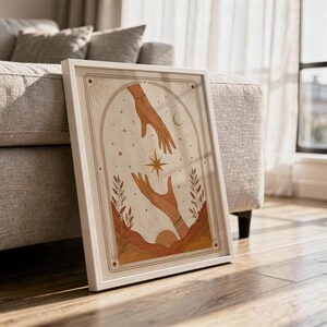 Terracotta celestial hands print framed on hardwood floor in sunlit living room decor.