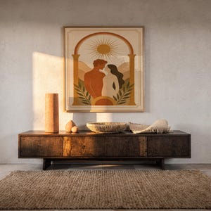 Framed minimalist sun and couple poster hanging above a dark wood sideboard console in a warm, ambient living room interior.