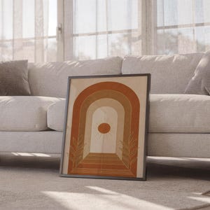 Boho arch sun wall art print leaning against a white sofa in a bright living room with sheer curtains.