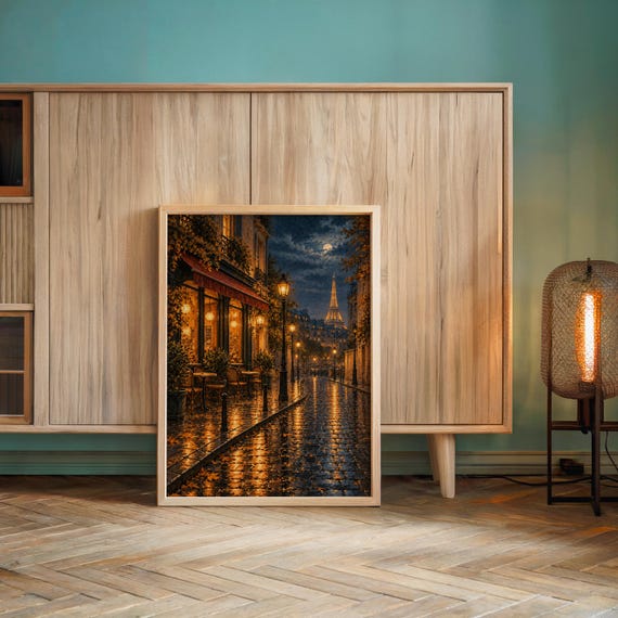 Paris eiffel tower wall art print leaning against a wooden cabinet by a teal wall beside a glowing floor lamp.