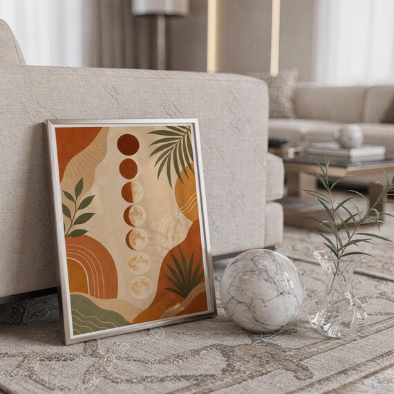 Boho moon phases art print in a silver frame leaning against a sofa beside a decorative marble sphere.