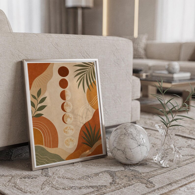 Boho moon phases art print in a silver frame leaning against a sofa beside a decorative marble sphere.