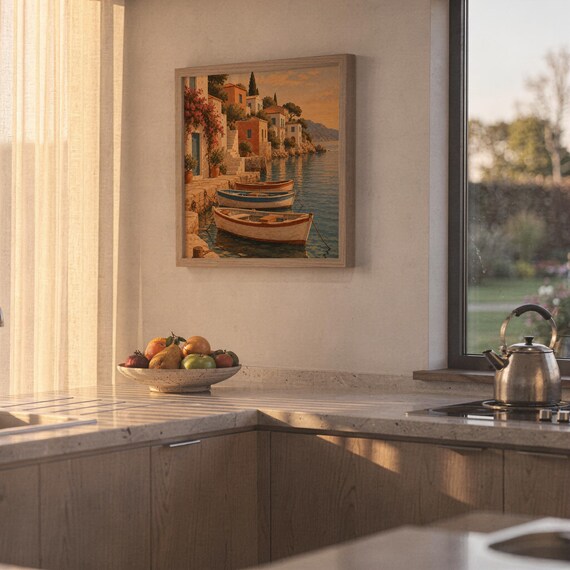 Mediterranean coastal village wall art print hanging above a stone countertop with a fruit bowl in a sunny kitchen.