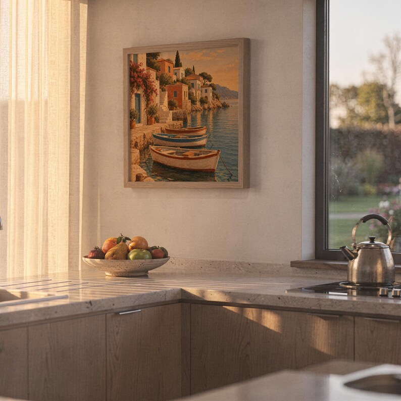 Mediterranean coastal village wall art print hanging above a stone countertop with a fruit bowl in a sunny kitchen.