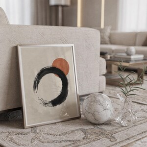 Framed Japanese brushstroke art leaning on the floor next to a white marble sphere.