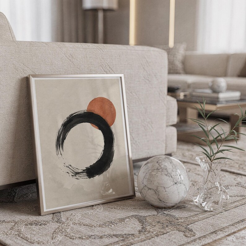 Framed Japanese brushstroke art leaning on the floor next to a white marble sphere.