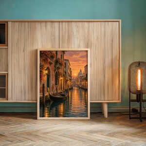 Venice canal sunset wall art print leaning against a wooden cabinet by a teal wall beside a glowing floor lamp.