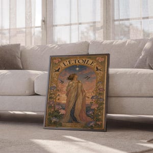 A dark-framed art nouveau L Etoile print resting on the floor between sections of a beige sectional sofa.