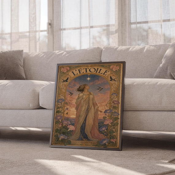 A dark-framed art nouveau L Etoile print resting on the floor between sections of a beige sectional sofa.