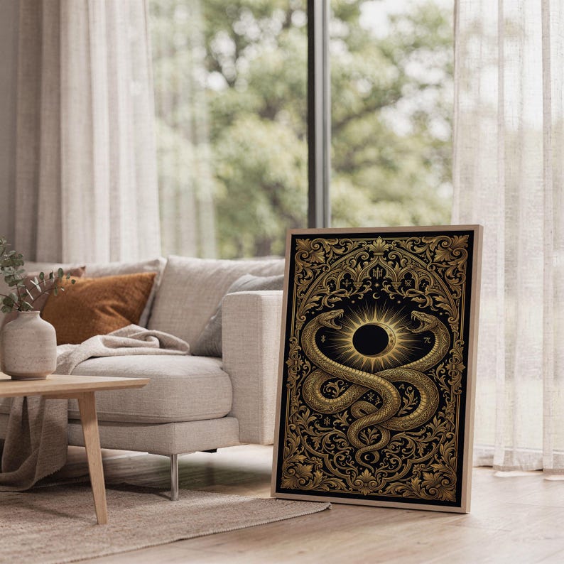 Occult snake wall art print leaning on the floor beside a cream armchair next to large garden windows.