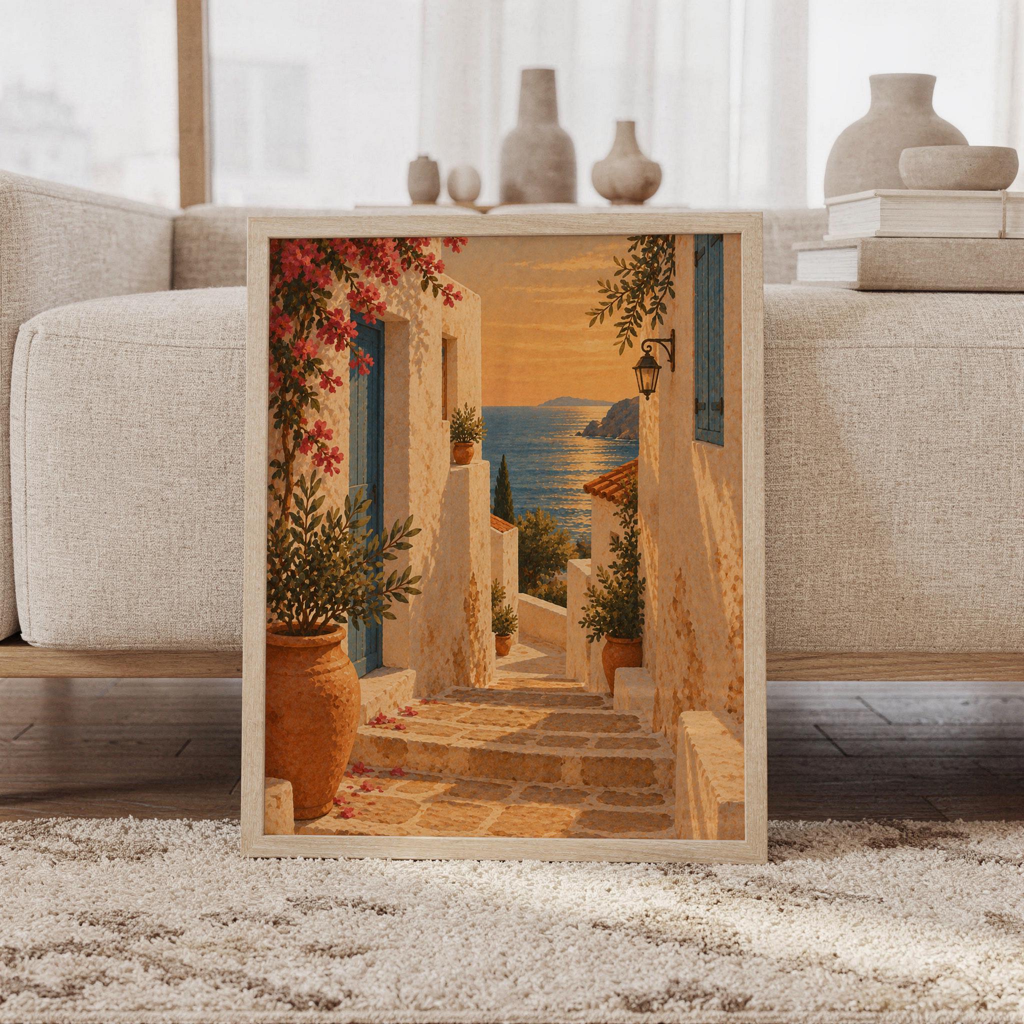 Mediterranean coastal village wall art print featuring warm golden sunset tones, ivory stone buildings, weathered blue doors, terracotta pots, and cascading pink bougainvillea framing a shimmering sea view, framed and leaning against a beige sofa on a textured rug in a bright Scandinavian living room.