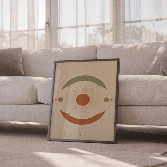Abstract sun wall art print leaning against a white sofa in a bright living room with sheer curtains.