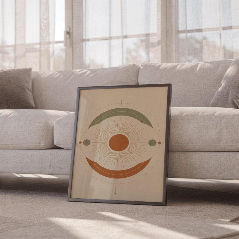 Abstract sun wall art print leaning against a white sofa in a bright living room with sheer curtains.