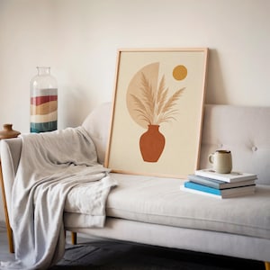 Single framed pampas grass in a terracotta vase art print displayed on a white sofa.
