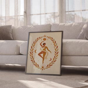Boho botanical dancer poster in a thin frame sitting on the carpet in front of a cozy white sofa in a bright living space.