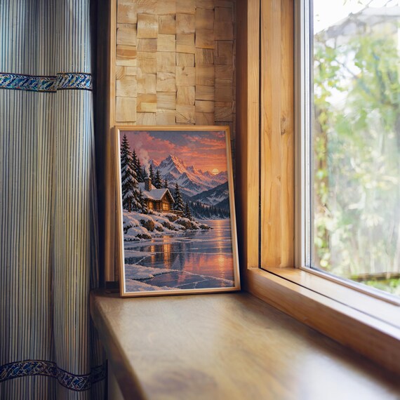 Winter cabin mountain wall art print standing on a wooden window sill in warm natural light.