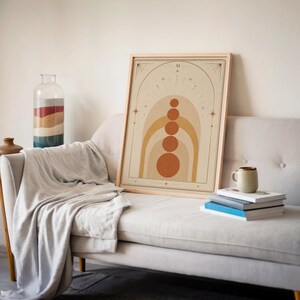 Mid century arch and circles print framed on beige sofa with blanket and books in living room decor.