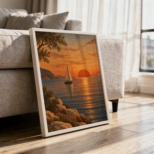 Sunset sailboat wall art print in a white frame leaning against a gray sofa on a sunlit wooden floor.