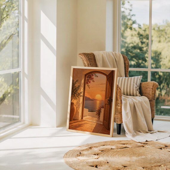 Mediterranean sunset doorway wall art print leaning on the floor beside a rattan armchair and jute rug in a bright sunlit room.