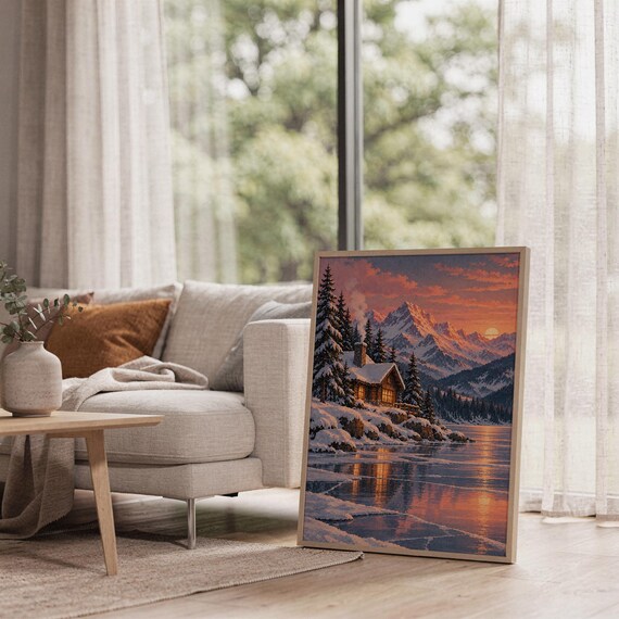 Winter cabin mountain wall art print leaning on the floor beside a cream armchair next to large garden windows.