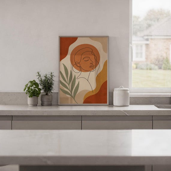 Abstract line art face print standing on a white kitchen counter beside potted herbs.