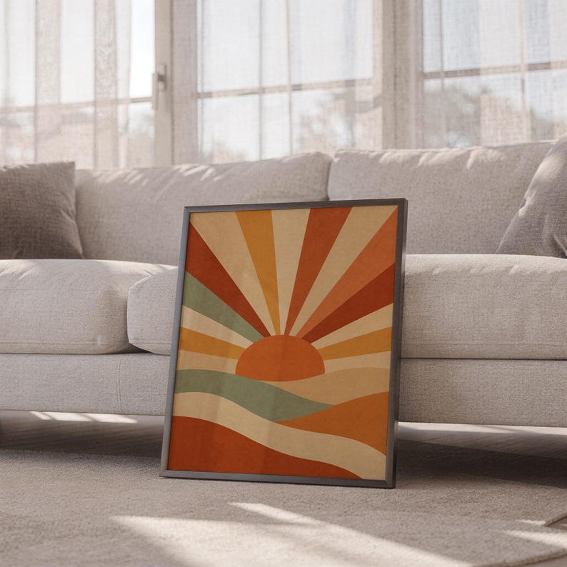 Retro geometric sunrise print leaning against a white sofa in a bright living room with sheer curtains.