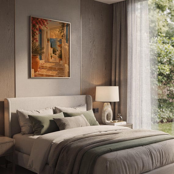 Mediterranean coastal village wall art print hanging above a bed with sage green pillows in a calm neutral bedroom.