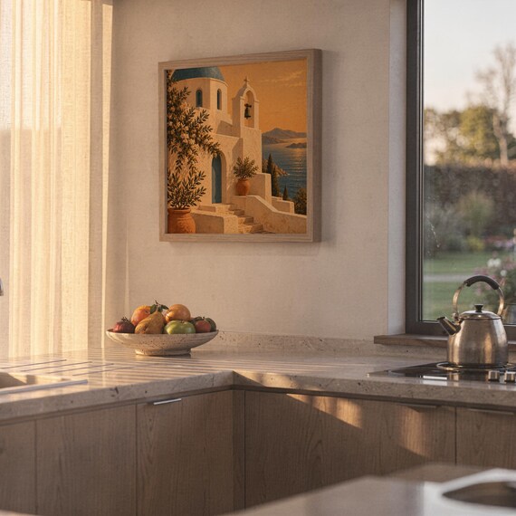 Santorini church wall art print hanging above a stone countertop with a fruit bowl in a sunny kitchen.