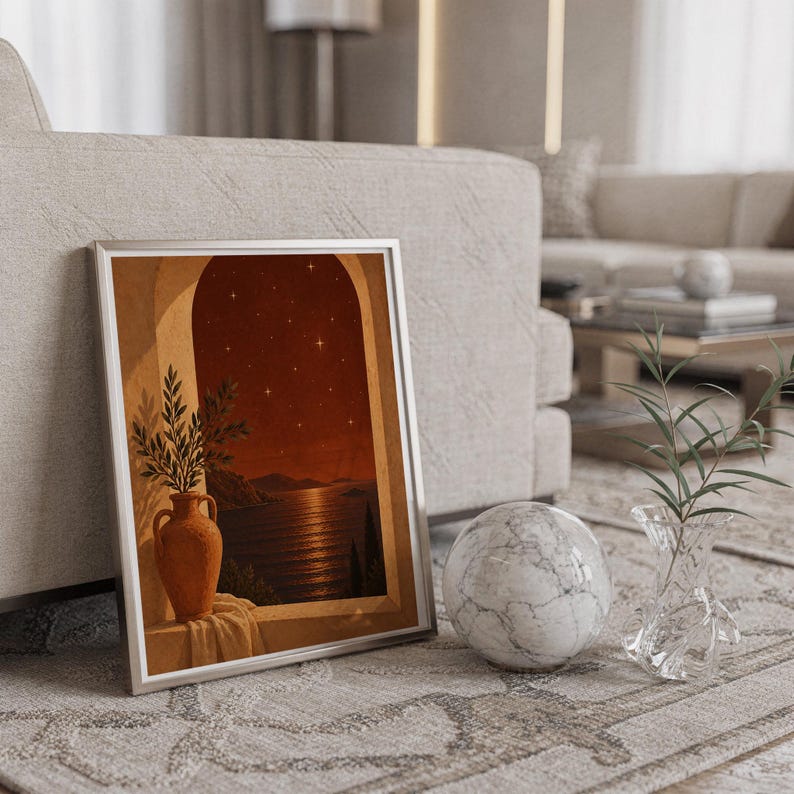 Mediterranean night sea wall art print in a silver frame leaning against a sofa beside a decorative marble sphere.