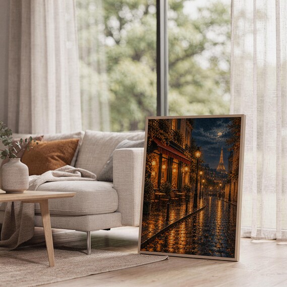 Paris eiffel tower wall art print leaning on the floor beside a cream armchair next to large garden windows.