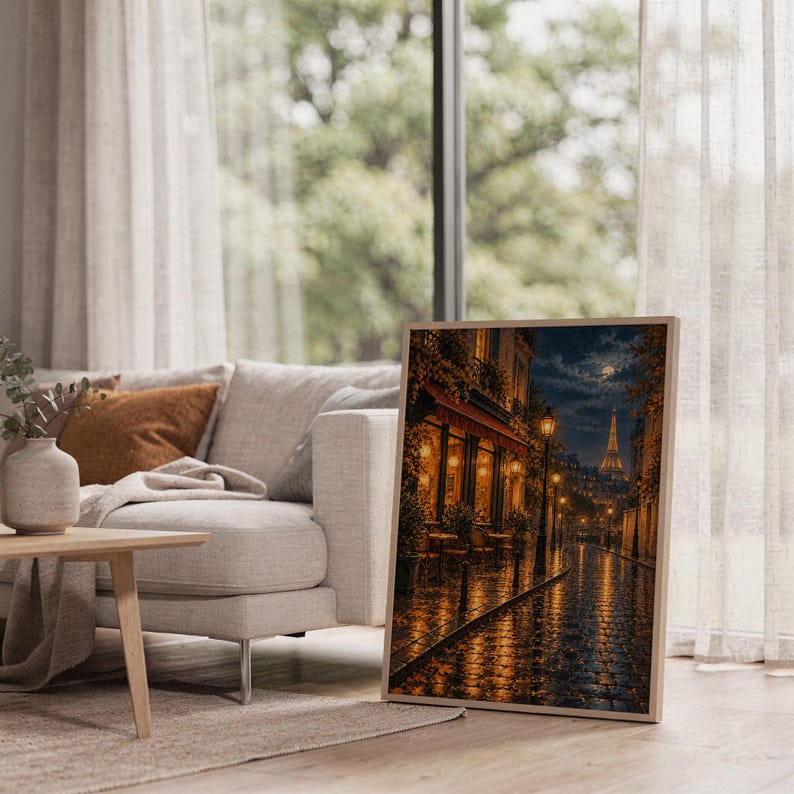 Paris eiffel tower wall art print leaning on the floor beside a cream armchair next to large garden windows.