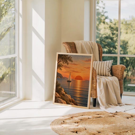Sunset sailboat wall art print leaning on the floor beside a rattan armchair and jute rug in a bright sunlit room.