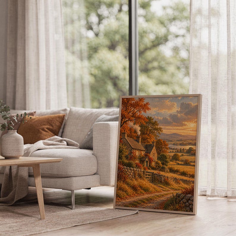 Autumn cottage landscape wall art print leaning on the floor beside a cream armchair next to large garden windows.