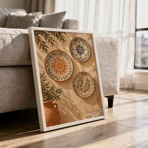 Mediterranean ceramic plate wall art print in a white frame leaning against a gray sofa on a sunlit wooden floor.