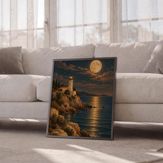 Moonlit lighthouse wall art print leaning against a white sofa in a bright living room with sheer curtains.