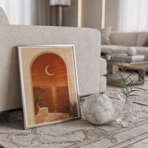 Mediterranean crescent moon arch print in a silver frame leaning against a sofa beside a decorative marble sphere.