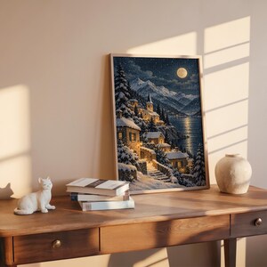 Snowy mountain village wall art print hanging above a bed with sage green pillows in a calm neutral bedroom.