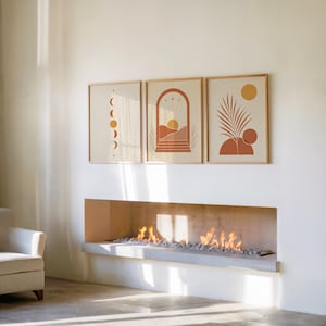 Set of 3 terracotta sun and moon phases wall art prints framed side by side above a modern indoor fireplace, creating a warm, cozy, and sophisticated living room gallery wall set focal point with soft ambient shadows.