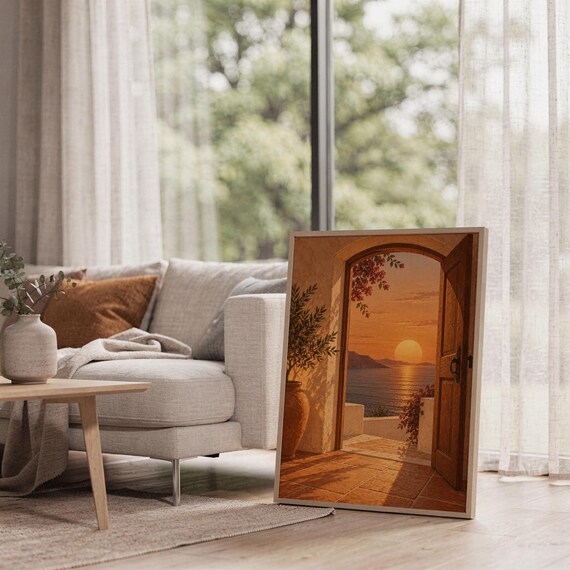 Mediterranean sunset doorway wall art print leaning on the floor beside a cream armchair next to large garden windows.