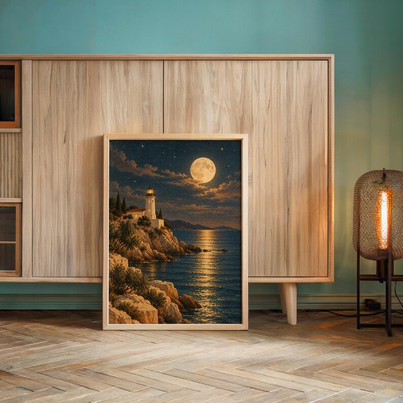 Moonlit lighthouse wall art print leaning against a wooden cabinet by a teal wall beside a glowing floor lamp.