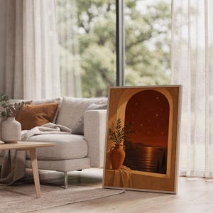 Mediterranean night sea wall art print leaning on the floor beside a cream armchair next to large garden windows.