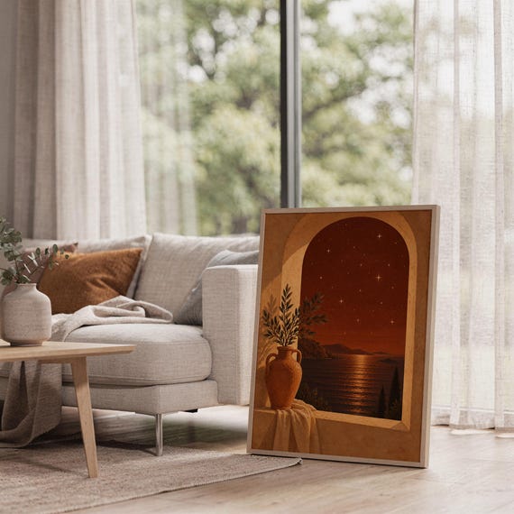 Mediterranean night sea wall art print leaning on the floor beside a cream armchair next to large garden windows.