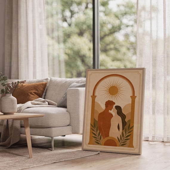 Framed boho wall decor leaning on the floor beside a sofa and large window with natural light illuminating the minimalist room.