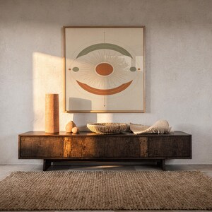 Abstract sun wall art print hanging above a dark wood console and jute rug in a warm neutral interior.