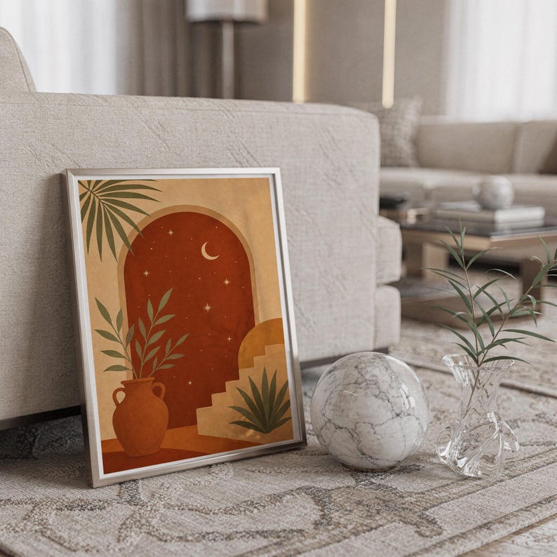 Terracotta moon and stars arch art print in a silver frame leaning against a sofa beside a decorative marble sphere.