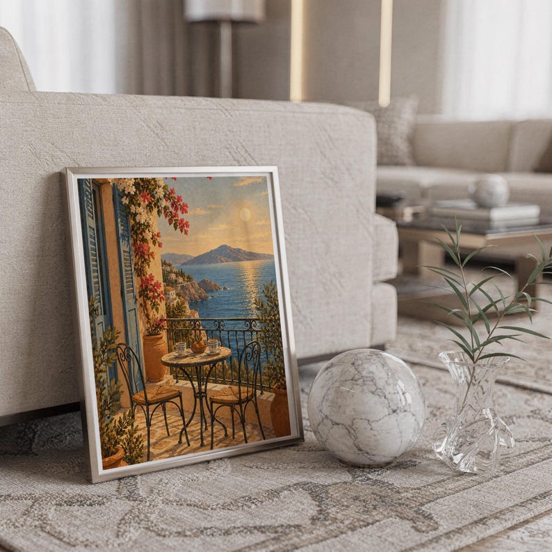 Mediterranean balcony wall art print in a silver frame leaning against a sofa beside a decorative marble sphere.