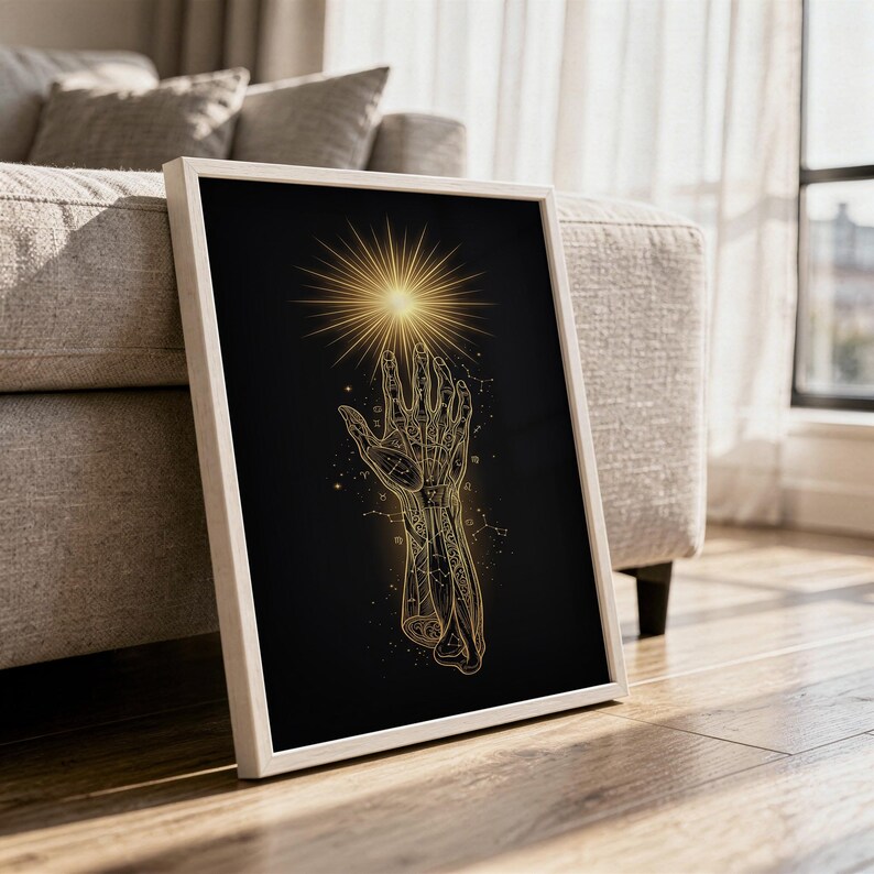 Celestial hand wall art print in a white frame leaning against a gray sofa on a sunlit wooden floor.