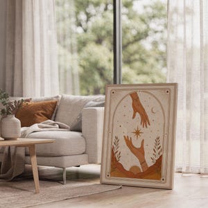 Boho celestial star and hands poster framed on bright sunlit living room floor next to window.
