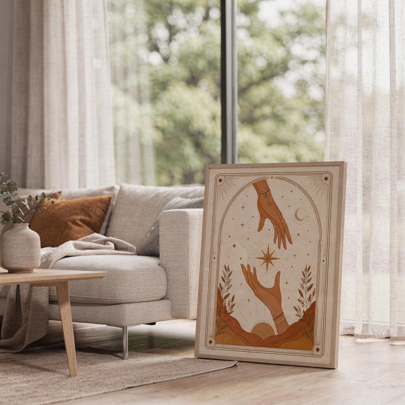 Boho celestial star and hands poster framed on bright sunlit living room floor next to window.