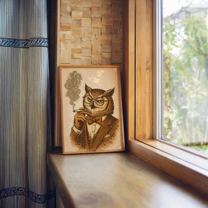 A framed print of an owl in a brown suit, red bow tie, and glasses, smoking a cigar with smoke curling up, sits on a wooden windowsill next to a striped curtain.